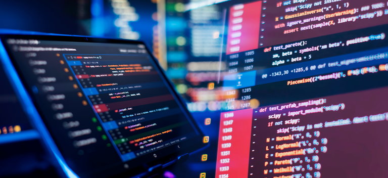 Programmiercode auf Bildschirm Ein Laptop-Bildschirm zeigt einen Code-Editor mit farblich hervorgehobenem Programmiercode. Im Hintergrund sind verschwommene digitale Elemente und weitere Bildschirme sichtbar, die eine technische Umgebung verdeutlichen.